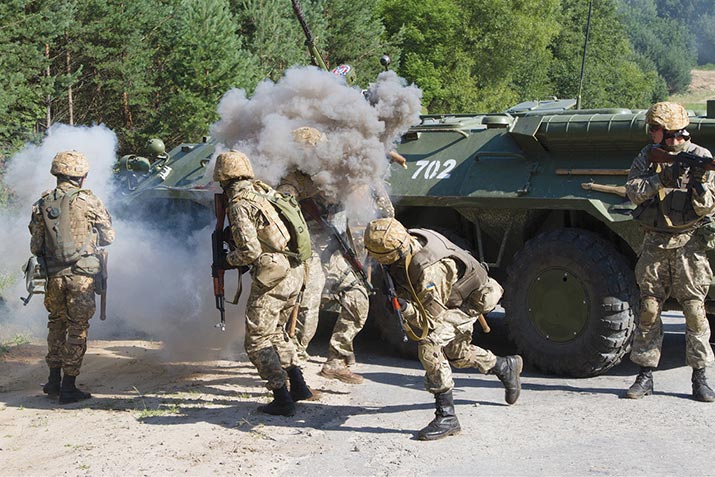An instructor with the Armed Forces of Ukraine (center) throws a smoke grenade on top of a BTR-80 armored personnel carrier