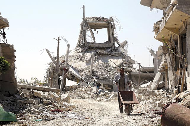 A Syrian man pushes a wheelbarrow past collapsed buildings 14 August 2016 in the northern Syrian town of Manbij