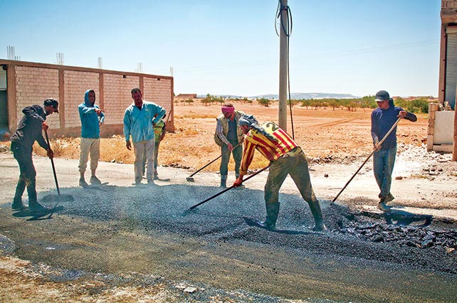 Men repair a road 11 July 2018 in a village outside Manbij, Syria.