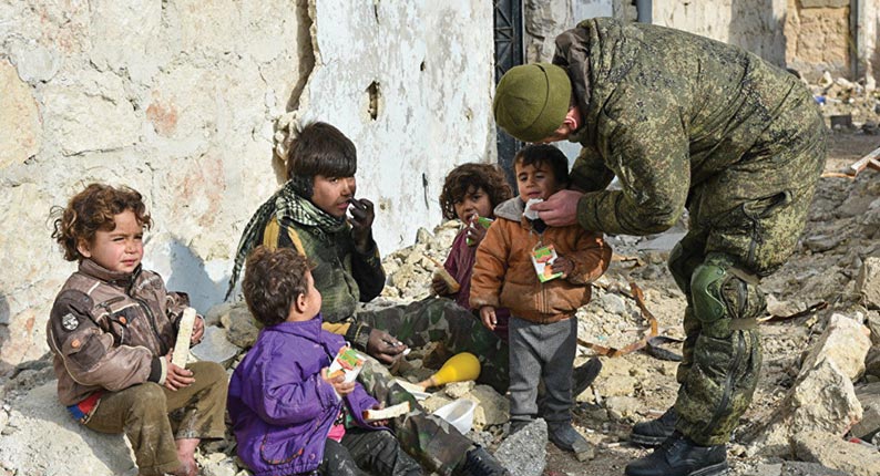 A Russian sapper administers relief to a group of destitute children 23 December 2016 in Aleppo, Syria