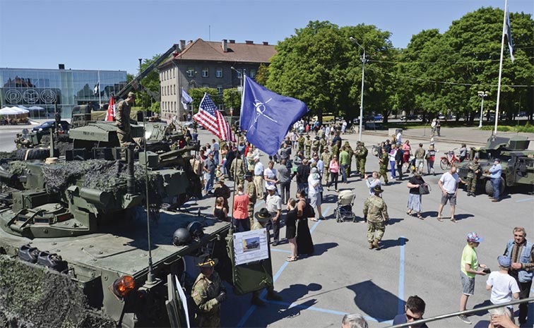 Hundreds of adults and children gather around the town center to look at Estonian, German, and U.S. military vehicles