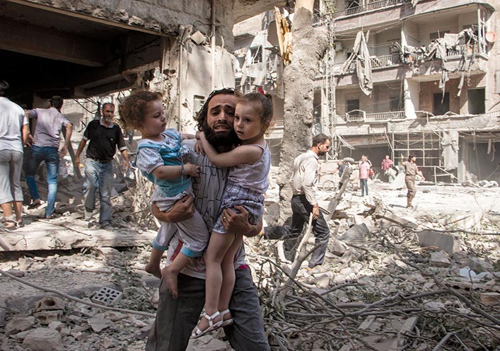 A Syrian man carries his two girls to safety 7 September 2015 across the rubble caused by a barrel bomb attack on the rebel-held neighborhood of al-Kalasa