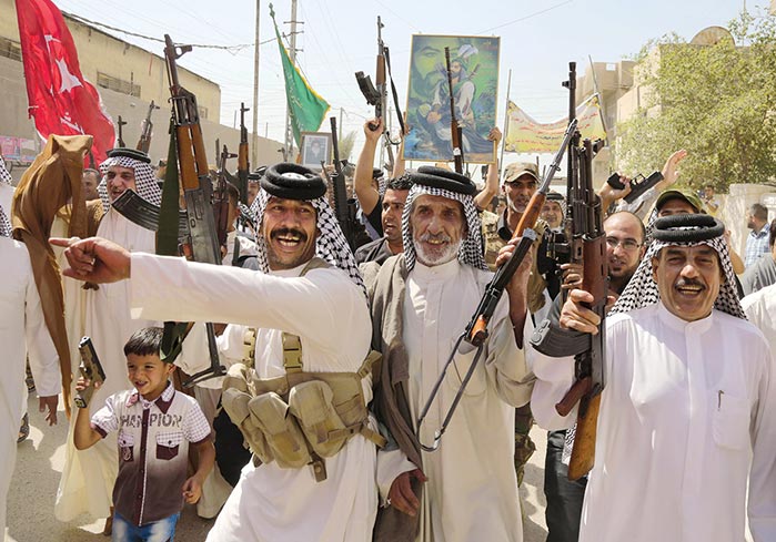 Iraqi Shiite tribal fighters raise their weapons while chanting slogans against the Islamic State 14 June 2014 in Baghdad's