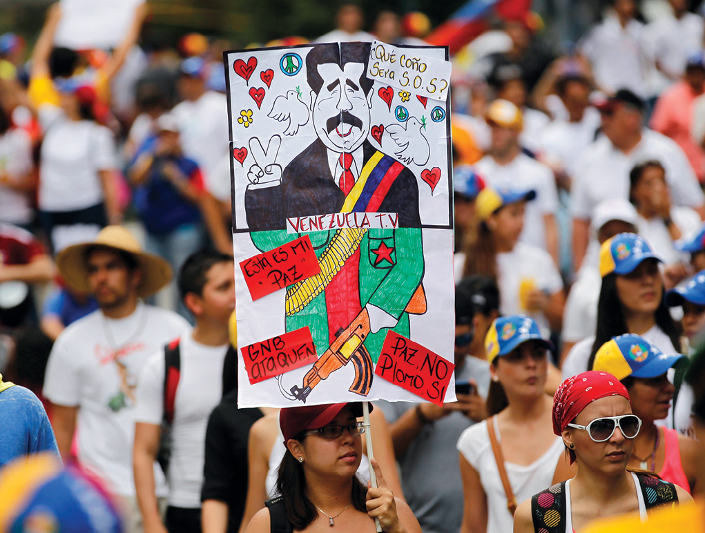 An antigovernment protester holds a poster with a caricature of Venezuela’s President Nicolas Maduro 2 March 2014 during a rally against his government in Caracas. The poster reads, “What the hell does SOS mean?,” “Peace no, bullets yes.” Subsequently, thousands of antigovernment demonstrators marched in the capital trying to keep up the momentum during months of protests demanding Maduro's resignation. (Photo by Jorge Silva, Reuters)