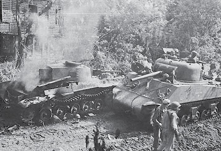 A Sherman tank passing a burning Japanese medium tank during World War II in Luzon, Philippines.