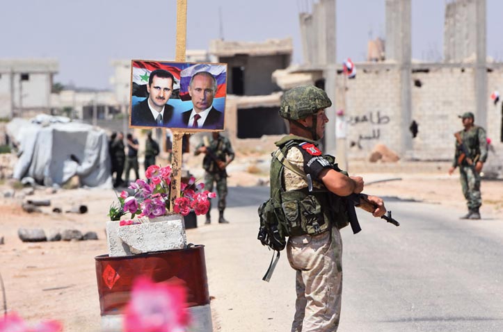 Members of Russian and Syrian forces stand guard near posters of Syrian President Bashar al-Assad and his Russian counterpart President Vladimir Putin