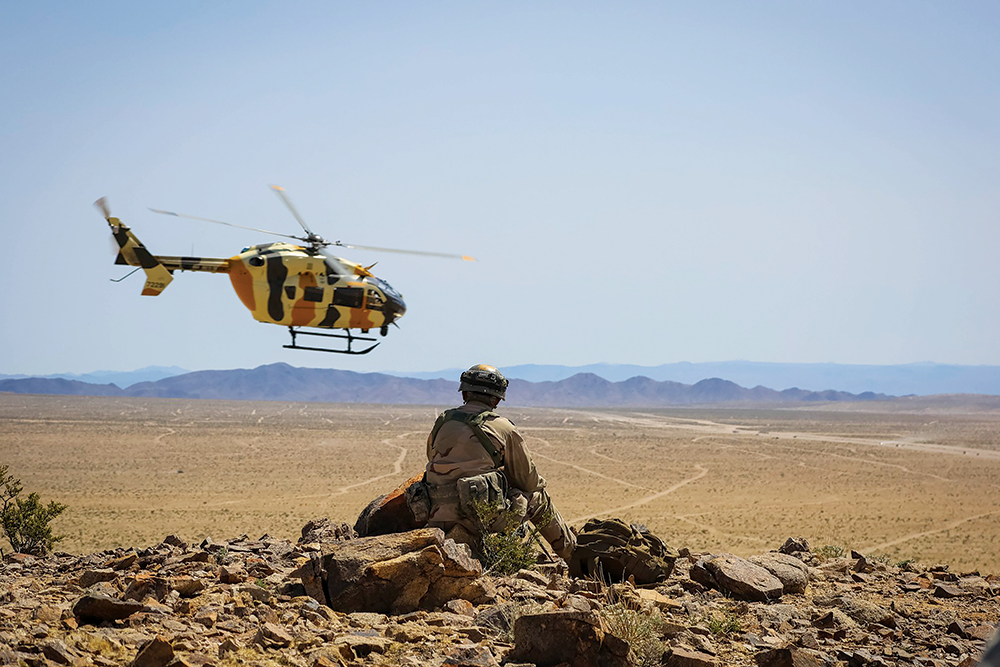 Um militar do 11o Regimento de Cavalaria Blindado observa o voo de um helicóptero UH-72 Lakota sobre o vale à sua frente, durante o Ciclo de Adestramento 18-06 de Ação Decisiva, no Centro Nacional de Treinamento, em Fort Irwin, Califórnia, 13 Abr 18. (Cb J. D. Sacharok, Grupo de Operações, Centro Nacional de Treinamento, Exército dos EUA)