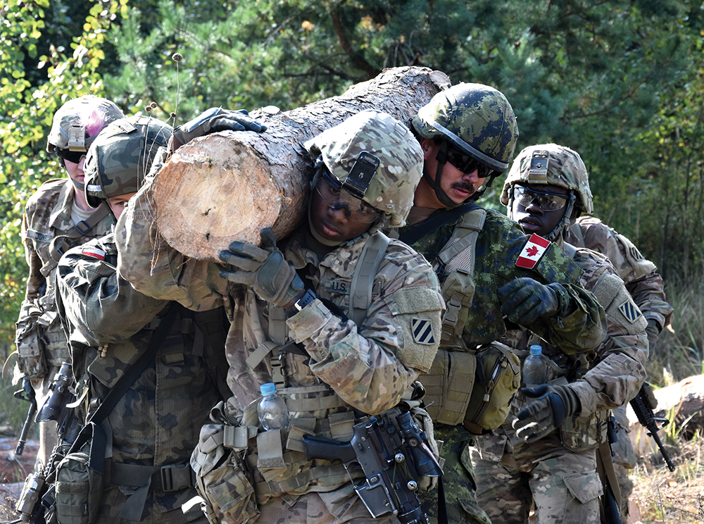 Militares da 3a Divisão de Infantaria do Exército dos EUA, junto com parceiros canadenses e poloneses, carregam um tronco de madeira durante uma série de exercícios em Yavoriv, na Ucrânia, em 28 Set 16. Esses militares foram desdobrados no leste europeu em apoio ao Grupo Multinacional Conjunto de Treinamento-Ucrânia (JMTG-U, na sigla em inglês). O JMTG-U se concentra no desenvolvimento de capacidades sustentáveis e duradouras, bem como nos sistemas de treinamento das forças terrestres ucranianas. (Cb John Onuoha/Exército dos EUA)