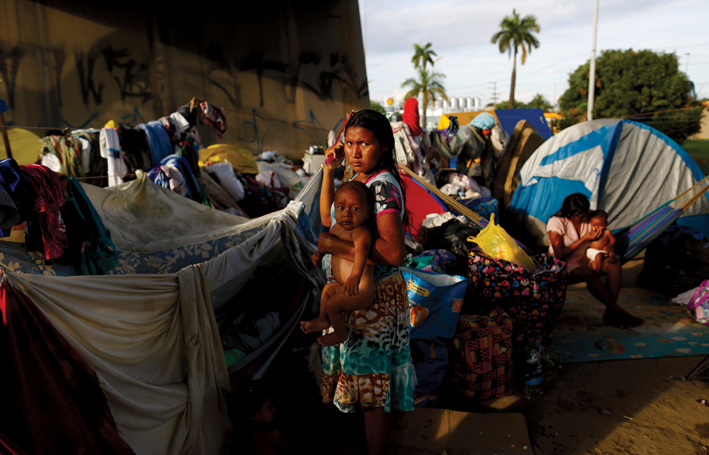 Mãe e filho de etnia Warao ao lado de um viaduto próximo a uma estação de ônibus em Manaus. Enfrentando a fome e privações em suas aldeias ao longo da costa caribenha, centenas de Warao vêm tentando a sorte nas ruas de Manaus. (Foto de Bruno Kelly, Reuters)