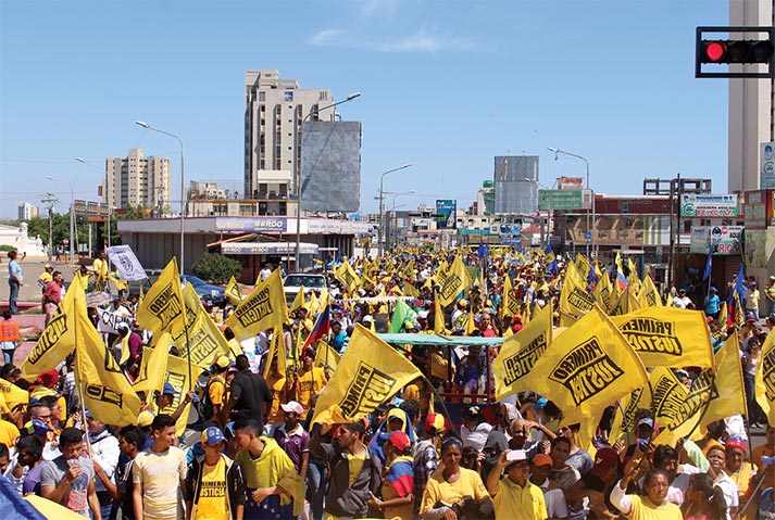 Cidadãos venezuelanos portando bandeiras com o texto “Primero Justicia”