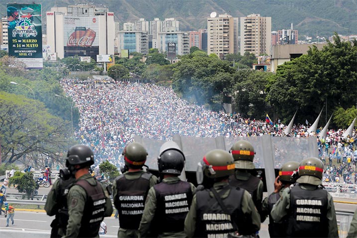 Integrantes da Guarda Nacional venezuelana observam uma manifestação contra o governo que ruma em direção à Assembleia Nacional em Caracas