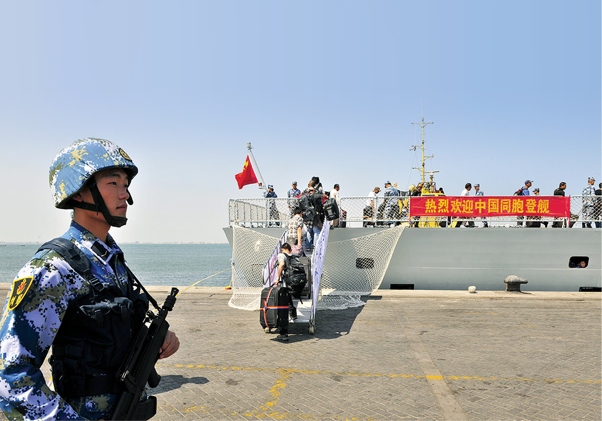 Un soldado chino de la Armada del EPL de guardia mientras ciudadanos embarcan el buque naval <i>Linyi</i> en el puerto de Adén, Yemen, 29 de marzo de 2015. El Ministerio de Defensa de China informó que sus buques de guerra habían llevado a cabo una evacuación de ciudadanos chinos con más de 570 transportados con seguridad a través del mar Rojo a Yibuti y después por avión a casa. Los caracteres chinos en el estandarte dicen: «Bienvenidos compatriotas chinos a bordo». (Foto: corresponsal, Reuters)