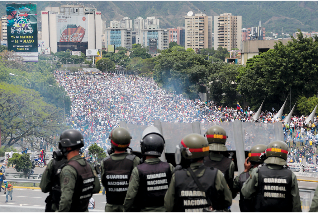 Soldados de la Guardia Nacional venezolana parados en una carretera el 3 de mayo de 2017 observan una manifestación contra el Gobierno que se dirige a la Asamblea Nacional en Caracas, Venezuela. Más de trescientos manifestantes fueron detenidos y llevados a tribunales militares esa semana, un auge repentino en el empleo de una práctica que, según activistas legales, viola la Constitución ya que la cortes militares se limitan a «ofensas de carácter militar». (Foto: Fernando Llano, Associated Press)