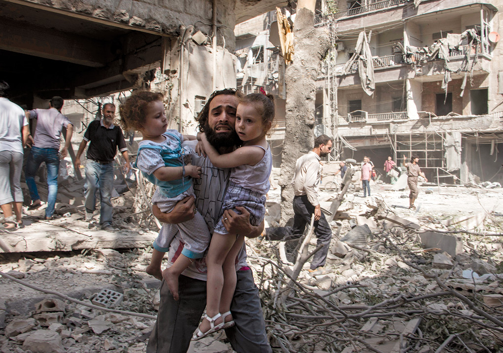 Un hombre sirio lleva a sus dos hijas a un lugar seguro en medio de los escombros causados por un ataque con bomba de barril en el vecindario controlado por los rebeldes de al-Kalasa en la ciudad norteña de Alepo, 7 de septiembre de 2015. Lo que en su día fuera el motor económico de Siria, Alepo fue destruido por el combate después de que los rebeldes tomaran control de la parte oriental de la ciudad en 2012, limitando a las fuerzas gubernamentales al oeste. Como resultado del gran número de muertes civiles debido a este tipo de bombardeo, Rusia y Siria recibieron la condena internacional por los ataques aéreos contra Alepo y otros blancos urbanos. (Foto: Karam al-Masri, Agence France-Presse)