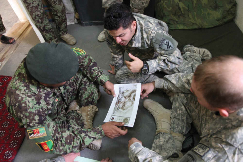 El sargento 1o Sediq Kamran del Ejército Nacional de Afganistán (izquierda) habla con Sal Jan (centro), un civil del Departamento de Defensa de EUA y el sargento 2o Kartton Killebrew de la 344a Compañía de Operaciones Psicológicas en el Campamento Lindsey, provincia de Kandahar, Afganistán, 28 de octubre de 2010. Killebrew discutió la propaganda creada por su unidad para expresar un mensaje de paz a los habitantes del área. (Foto: Cabo Robert Thaler, Ejército de EUA)