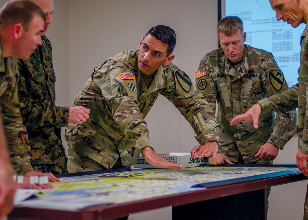 El mayor Lázaro Oliva Jr. (centro) discute con otros planificadores de la 1a División de Caballería las posibles consecuencias de una decisión táctica durante un juego de guerra el 8 de noviembre de 2018 en Fort Hood, Texas. Los juegos de guerra ayudan a mejorar la toma de decisiones y fortalecer la confianza entre las unidades. (Foto: Mayor Joseph Payton, Ejército de EUA)