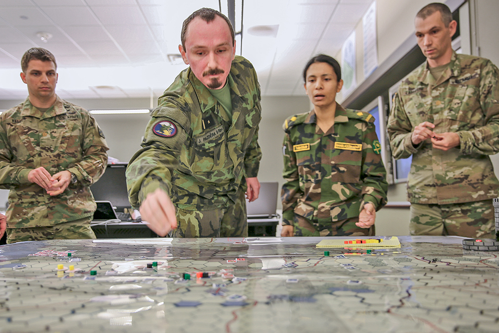 El mayor Jiri «Jorge» Pazdera del Ejército checo (centro) mueve marcadores en el mapa de Landpower, un ejercicio de simulacro que se lleva a cabo en un juego de mesa, mientras observan el mayor Adam Keller (izq.), la mayor Tasnuva Tabassum de Bangladesh y el mayor Zachary Labrayere (der.), el 9 de marzo de 2018 en la Escuela de Comando y Estado Mayor del Ejército de EUA en Fort Leavenworth, estado de Kansas. Se sometió al Landpower a una prueba piloto para determinar si es un reemplazo adecuado para los simulacros computarizados actuales en la escuela que toman mucho más tiempo para enseñar. (Foto: Capitán Charlie Dietz, Ejército de EUA)