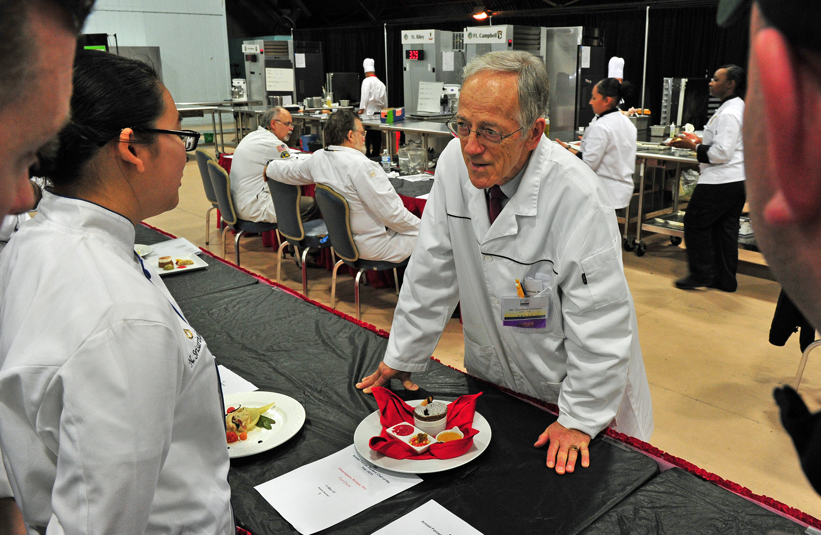 Pfc. Nichapa Srisaringkam is critiqued by American Culinary Federation judge Gunther Heiland as teammates look on. (U.S. Army photo by J.D. Leipold)