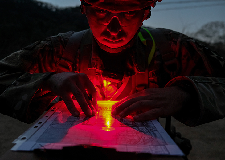 U.S. Army Staff Sgt. Symon Bowen, Delta Company, 2nd Battalion (Assault), 2nd Aviation Regiment, 2nd Combat Aviation Brigade, uses his red lens flashlight to plot points for night land navigation (TBA).
