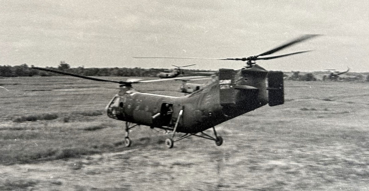 Tandem-rotor military helicopter hovering over a grassy field
