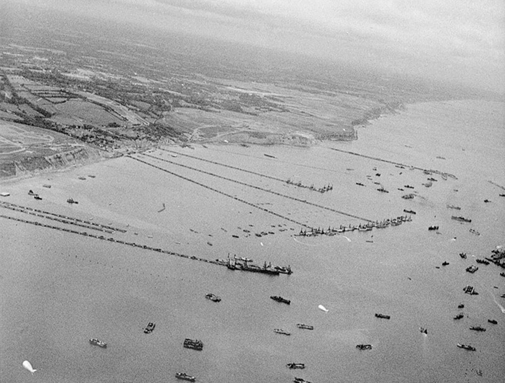 The image shows an aerial view of a historical D-Day landing site, with numerous ships and landing craft near a coastline, indicative of the massive scale of the Allied invasion during World War II.