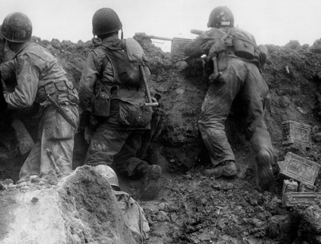 The image depicts World War II soldiers in helmets and combat gear climbing over a dirt mound, possibly during a battle or maneuver, with various military equipment visible on the ground.
