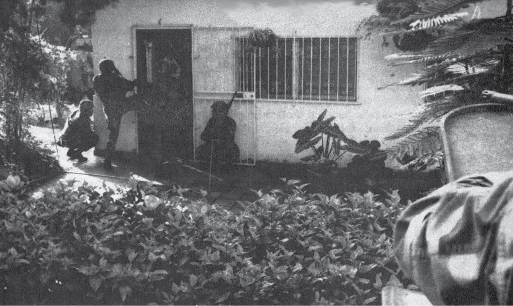 A Marine security team enters a house in Arrijan, Panama while other Marines in light armored vehicles watch its front and back, 20 December 1989.