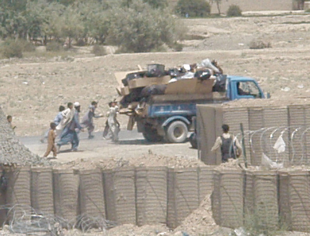 Afghan men and young boys attempt to grab bags of trash and pull them off a garbage truck