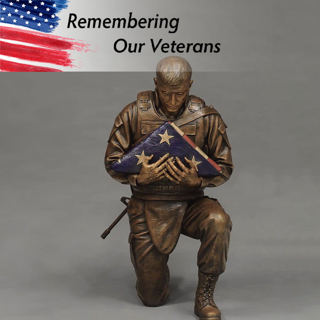 A statue of a soldier kneeling and reverently holding a folded American flag, with 'Remembering Our Veterans' written above and an American flag in the background.