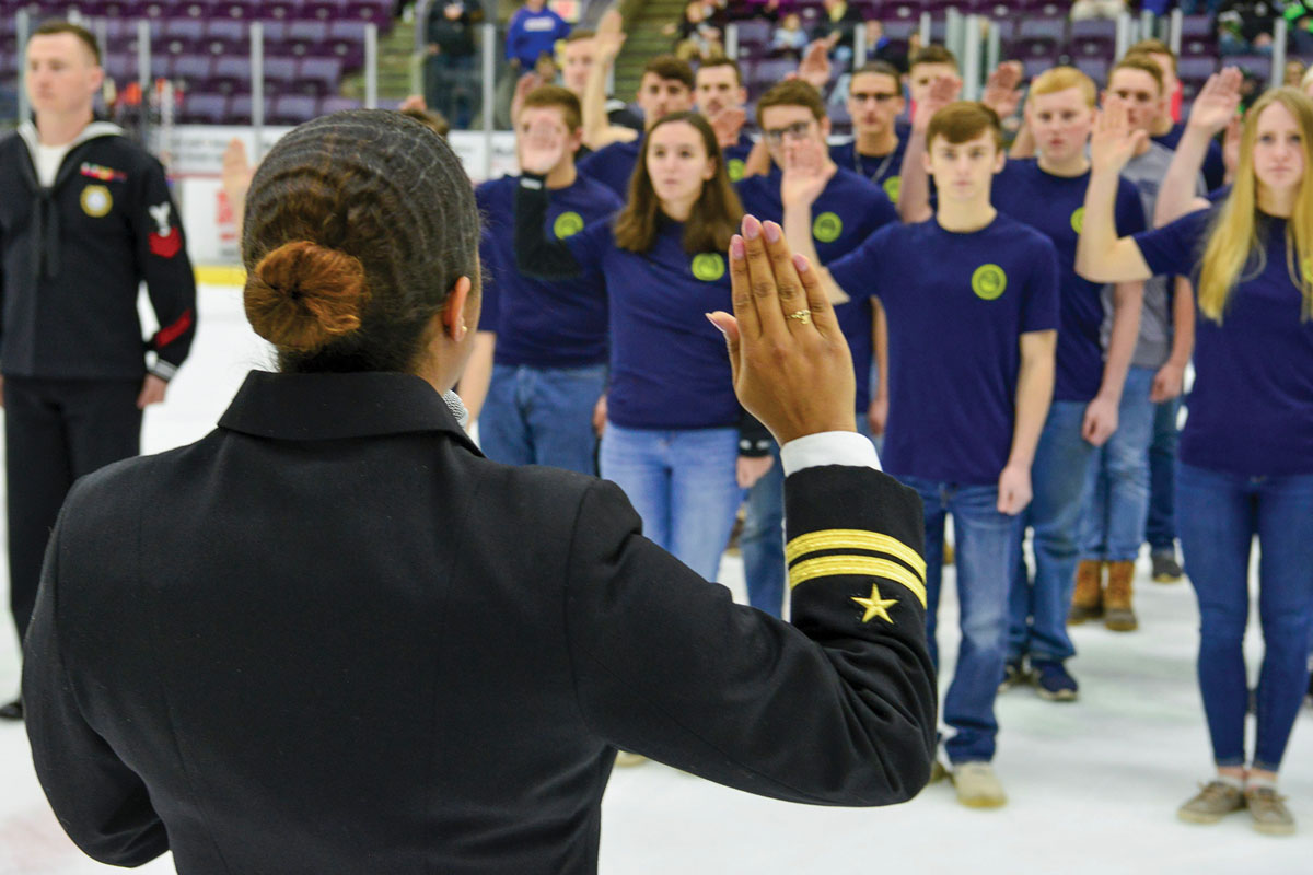 Navy Lt. Jade Reaves, officer in charge of Talent Acquisition Onboarding Center Syracuse, administers the oath of enlistment to twenty-three future sailors at an Elmira Enforcers hockey game in Elmira, New York, 27 February 2020