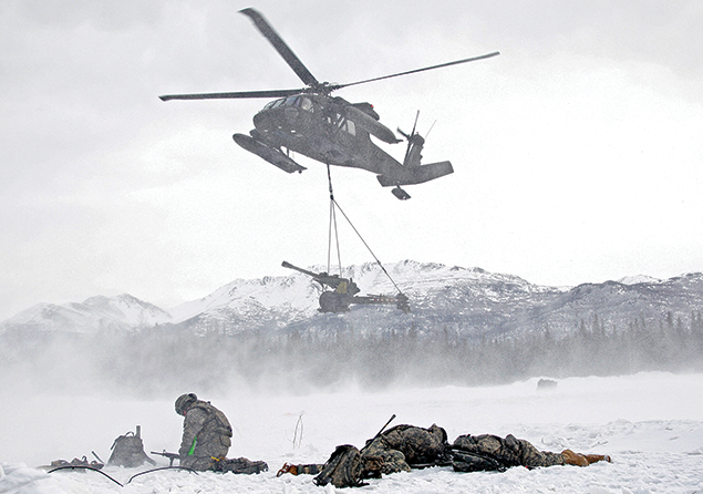 An Alaska Army National Guard UH-60 Black Hawk prepares to lower an M119A2 howitzer to soldiers