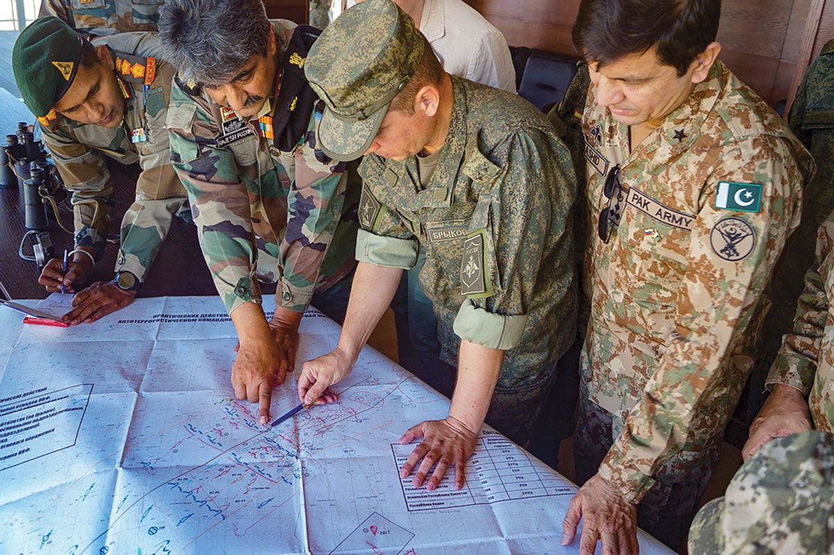 Military officers from different countries are gathered around a map, engaged in discussion. They are in uniform, indicating an international military collaboration or exercise.
