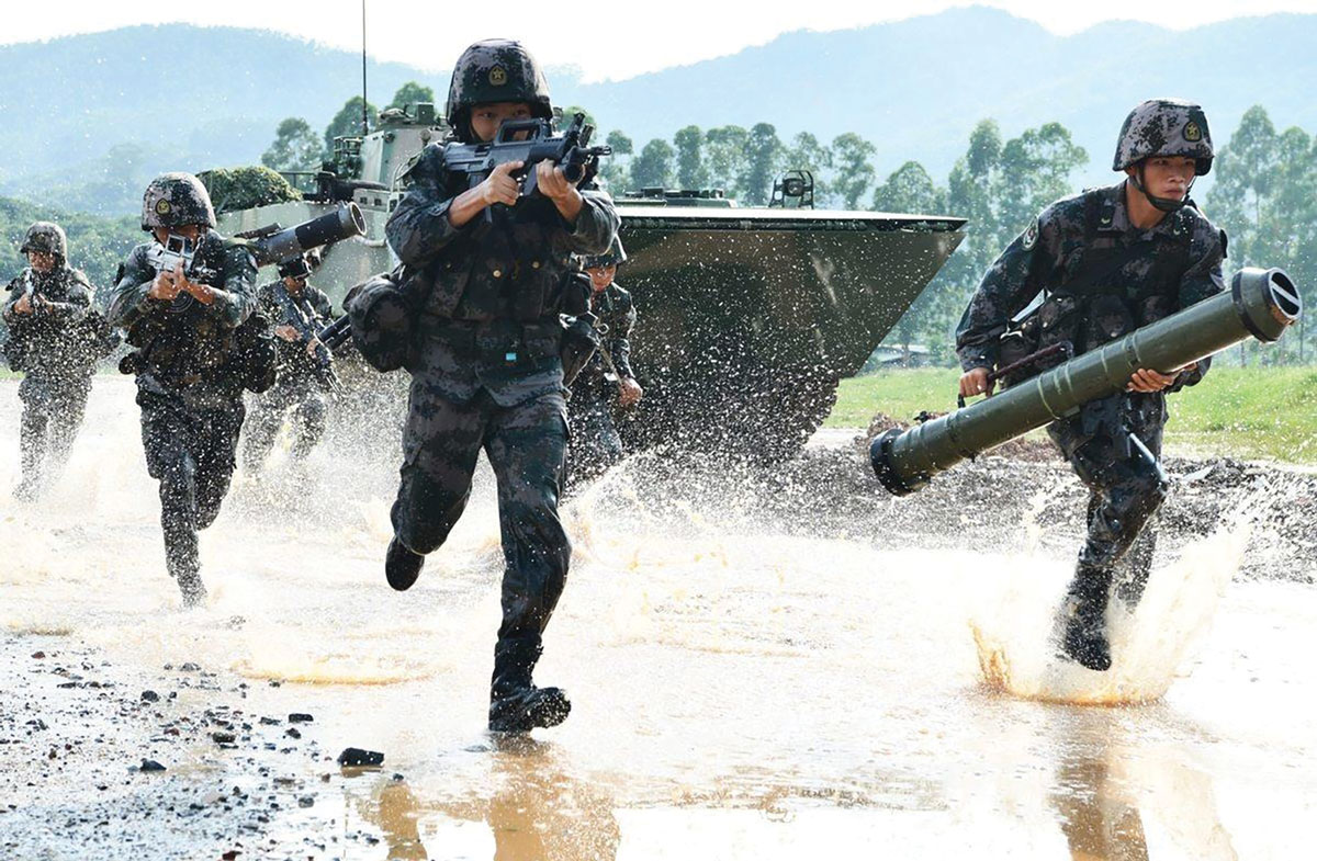 A squad of soldiers in camouflage uniforms sprinting through water with weapons ready, alongside an armored vehicle, in what appears to be a training exercise or rapid deployment scenario.