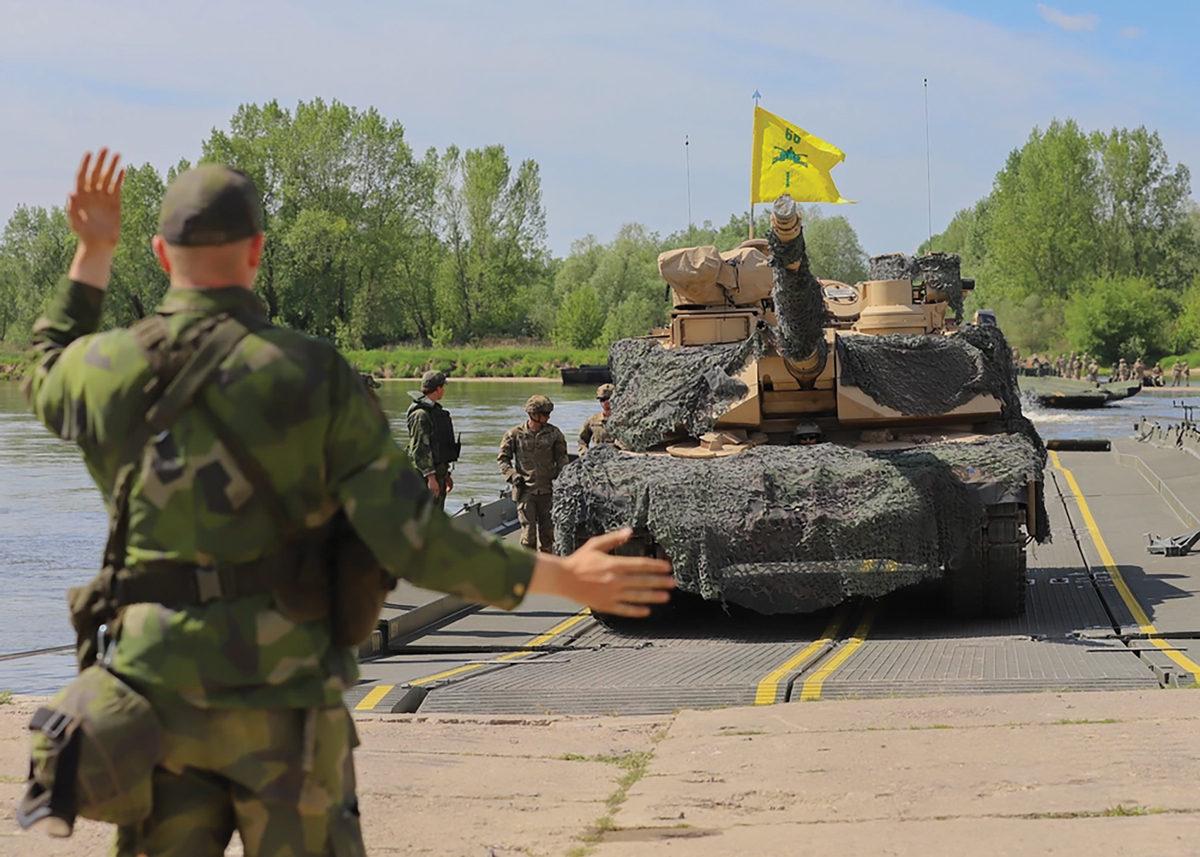 A Swedish soldier guides an M1A2 Abrams tank assigned to 1st Battalion, 66th Armored Regiment, 3rd Armored Brigade Combat Team, 4th Infantry Division, as it crosses the Vistula River 13 May 2022 during a wet-gap crossing at Dęblin, Poland, as part of Defender-Europe 22