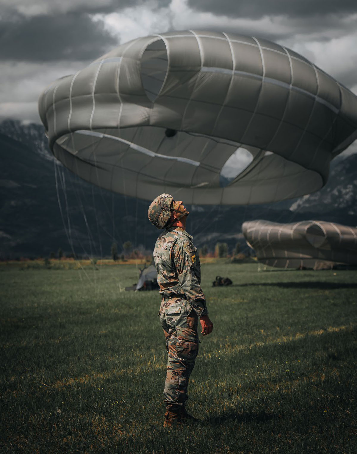 A U.S. Army paratrooper assigned to the 173rd Airborne Brigade looks up at the sky as fellow paratroopers descend to the ground during an airborne operation on Frida Drop Zone, Pordenone, Italy, 31 August 2023