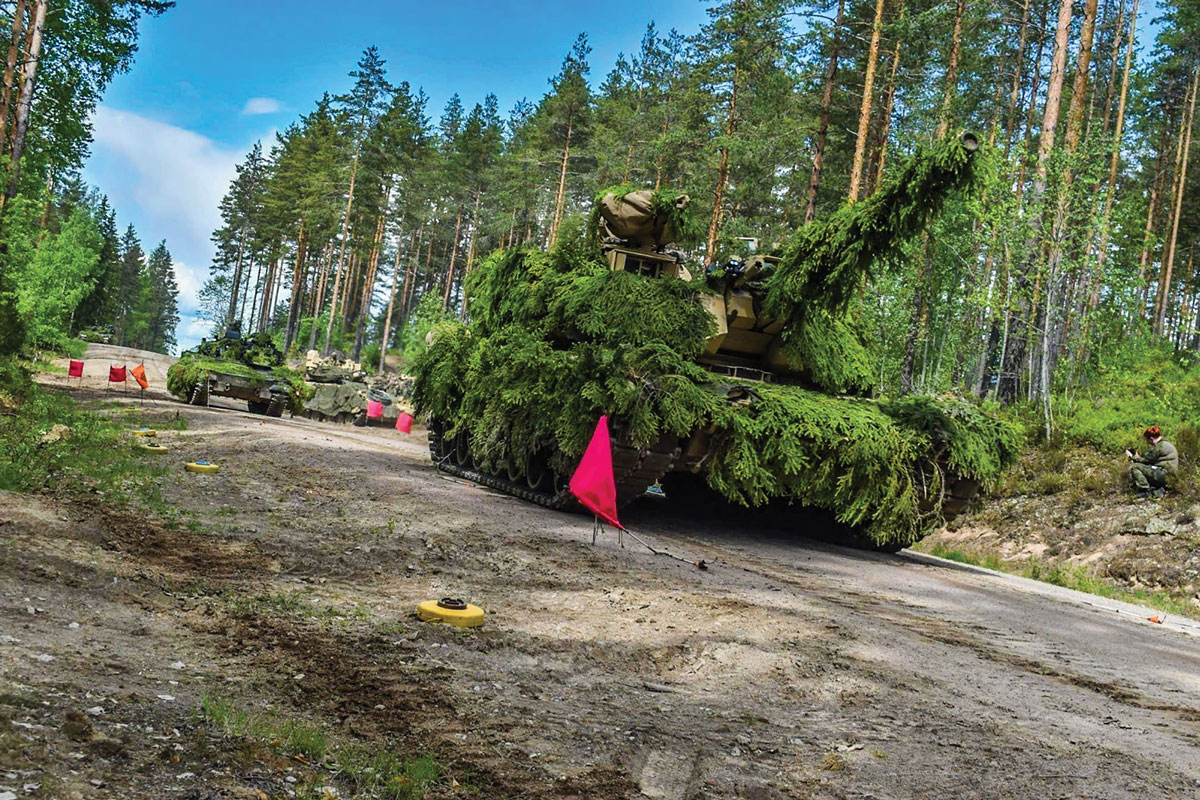 Heavily camouflaged M1A2 SEPv3 Abrams tanks from 1st Battalion, 8th Cavalry Regiment, 2nd Armored Brigade Combat Team, 1st Cavalry Division, move through a minefield on a cleared breach lane 27 May 2023 after being brought forward by dismounted scouts, infantry, and sappers in Vekaranjarvi, Finland, during Operation Lock