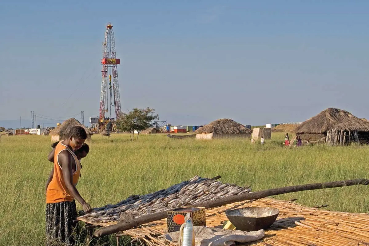  mother holds a baby while laying out fish to dry near an oil exploration rig by the shore of Lake Albert in northern Uganda, East Africa