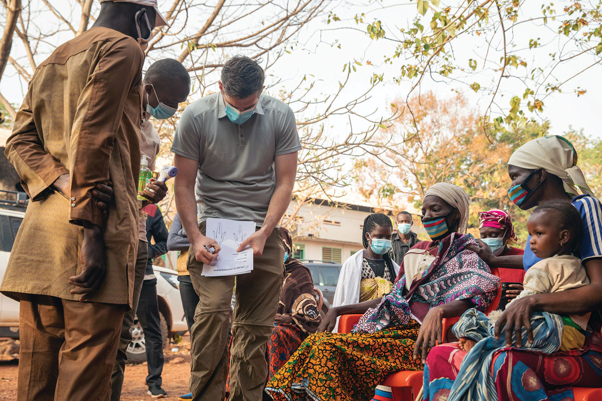 Staff Sgt. Aidan McNulty, Civil Affairs Team 142, Company D, 91st Civil Affairs Battalion and local residents with masks in a community setting, reviewing medical documents.