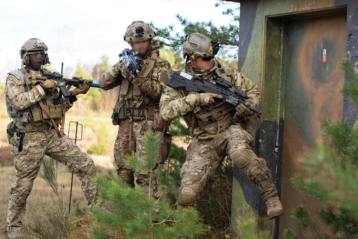 Three soldiers in tactical gear aim their weapons, preparing to breach a door in a training exercise.