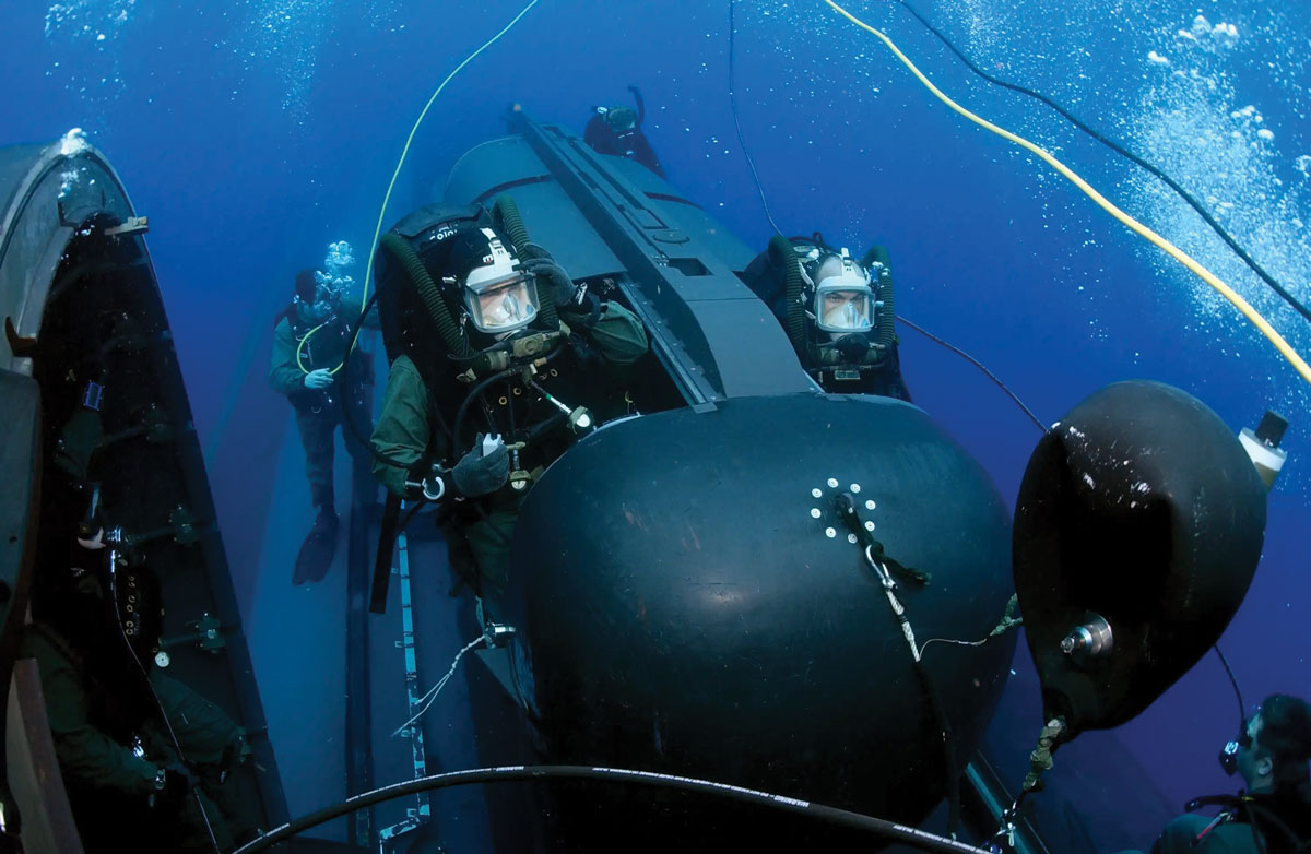 U.S. Navy SEAL Delivery Vehicle Team 2 divers in full gear conducting operations around a submerged SEAL Delivery Vehicle (mini submarine) in deep blue waters.