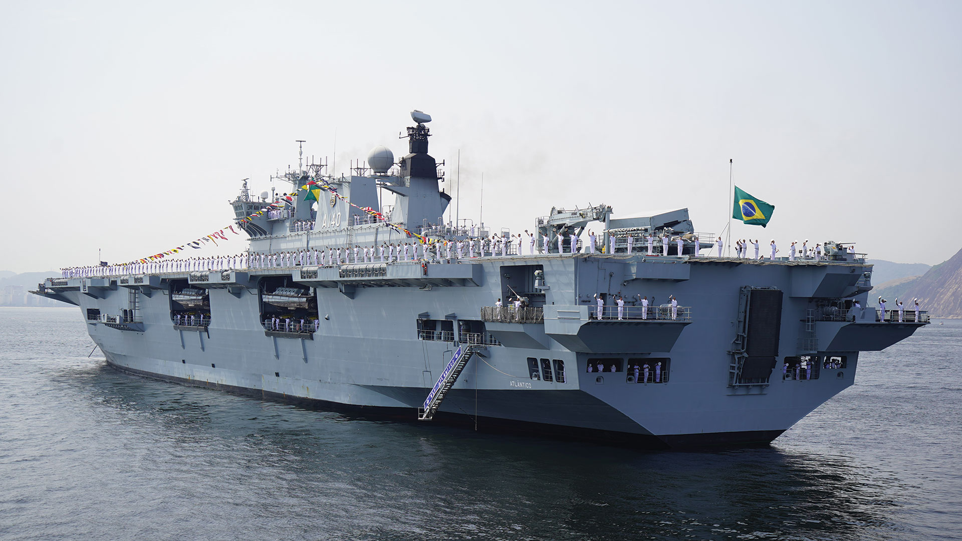 Brazilian Navy ship with uniformed sailors lining the deck, flying the national flag during a maritime ceremony.
