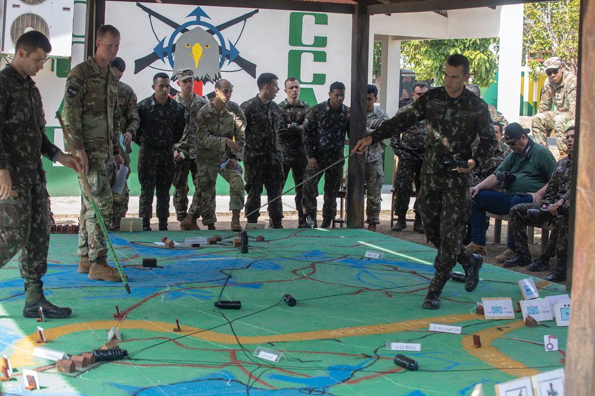 Brazilian and U.S. military personnel gathered around a large map on the ground for a joint strategy briefing or training exercise.