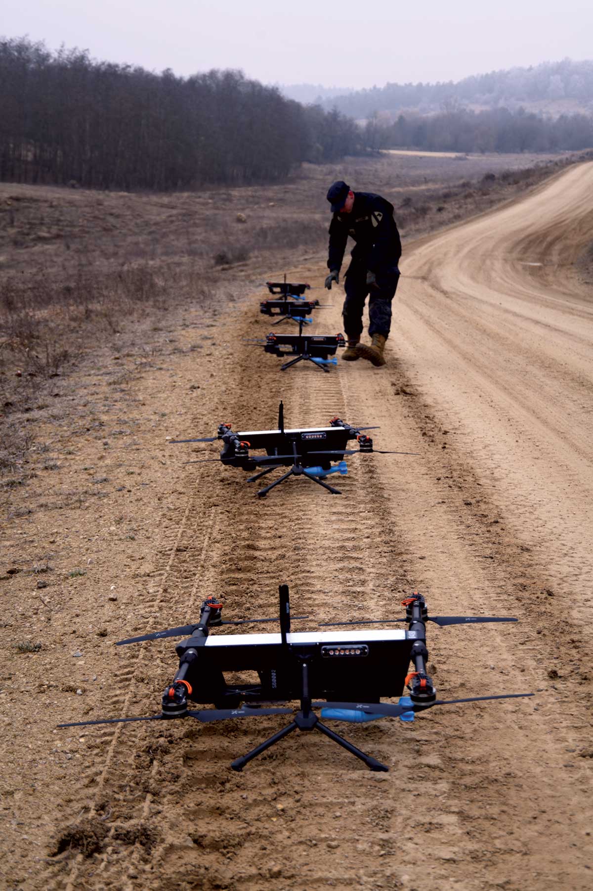 Line of quadcopter drones on a dirt road with an operator preparing them