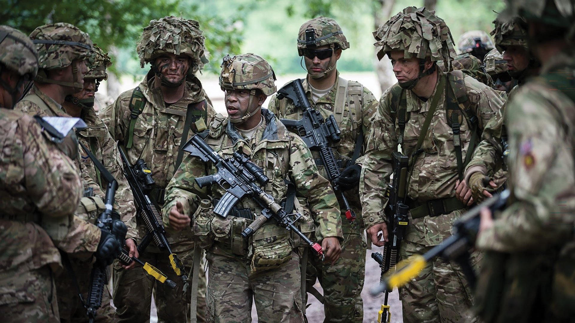 A group of soldiers with training rifles huddle together wearing face paint and camo