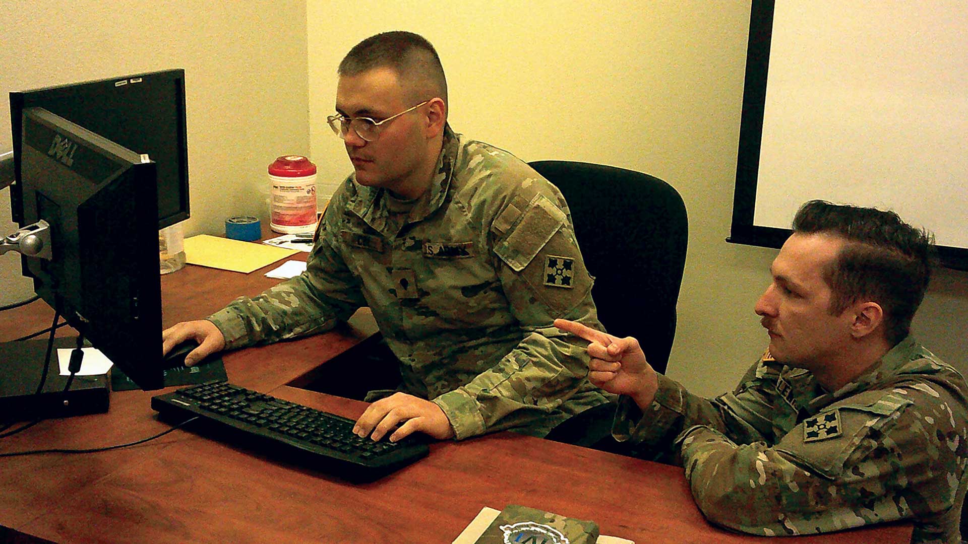 Two Soldiers sit by a computer