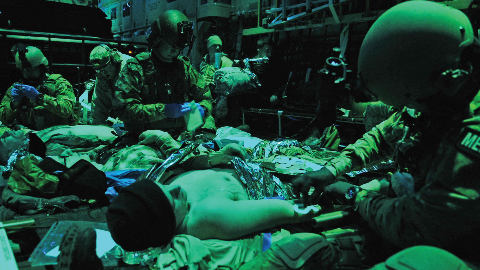 Combat medics aboard a military aircraft under green night vision lighting.