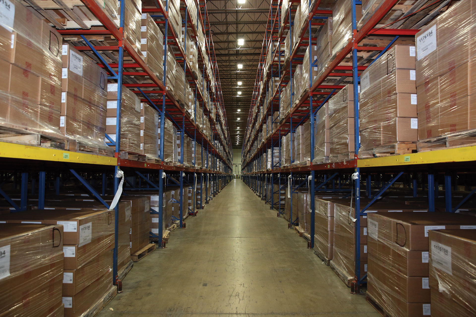 Interior view of a large warehouse with high shelves stacked with rows of shrink-wrapped boxes.