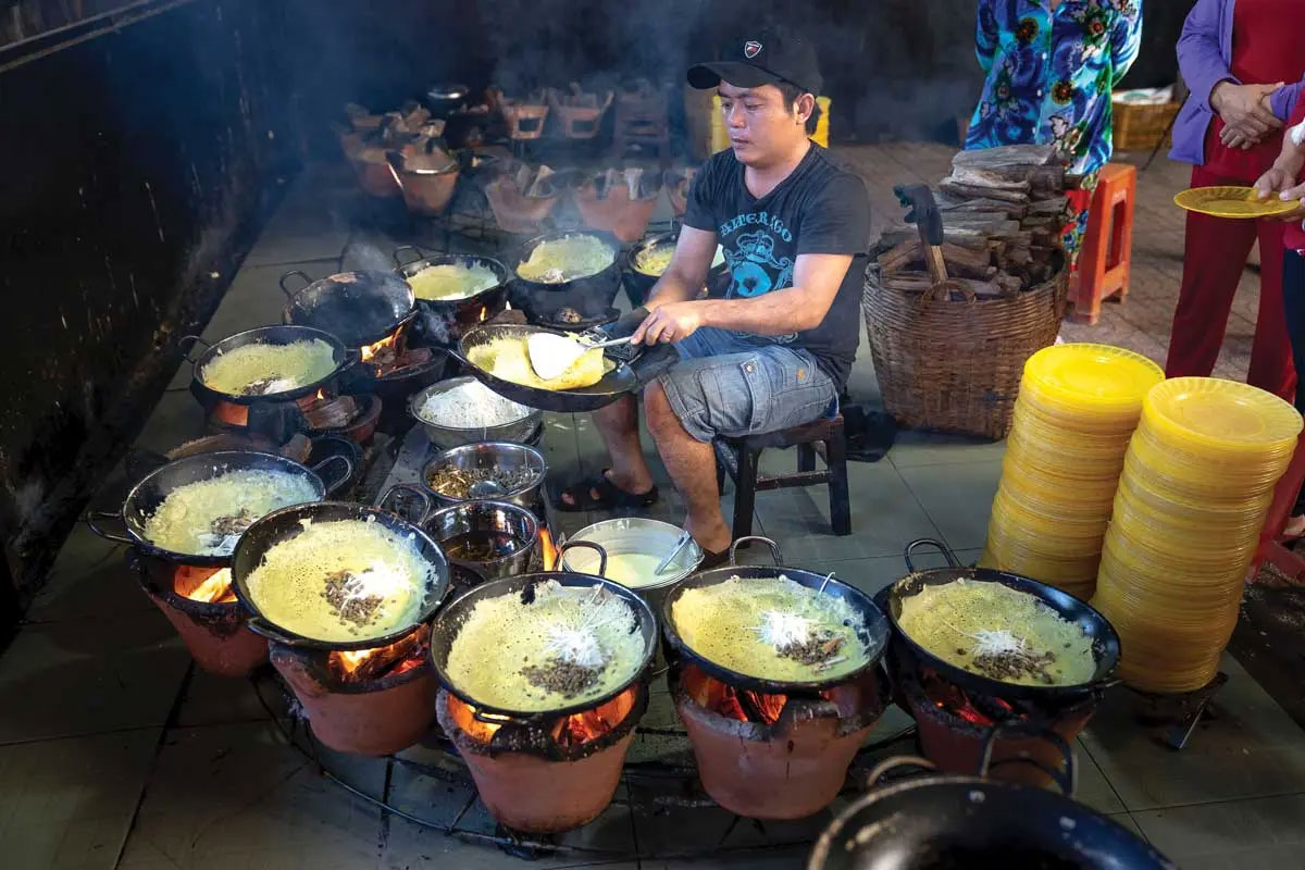 A Vietnamese man is shown cooking BÁnh xèo sizzling cake