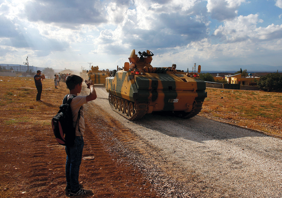 A boy salutes as Turkish army vehicles