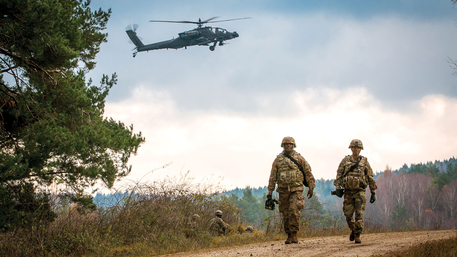 Soldiers walking down a dirt road with a helicopter in the background